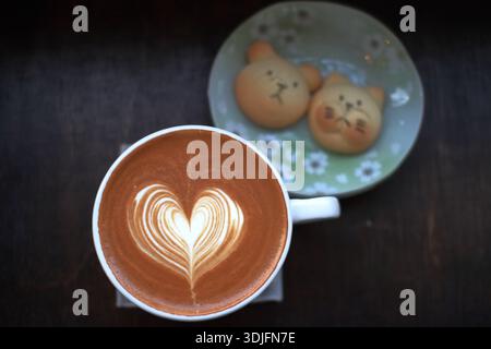 Tazza di latte con latte art a forma di cuore servito con biscotti su tavolo in legno, vista dall'alto. Foto Stock