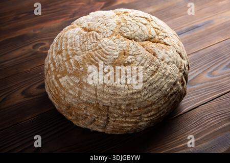 Pane fatto in casa rotondo appena sfornato con crosta dorata e croccante. Il pane presenta tagli caratteristici sulla superficie, che aggiungono al suo fascino rustico. Foto Stock