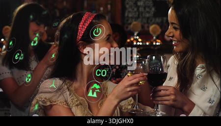 Bicchieri da vino, donne che indossano il top in pizzo e una camicetta con borchie sorridenti al bar, icone AR verdi Foto Stock