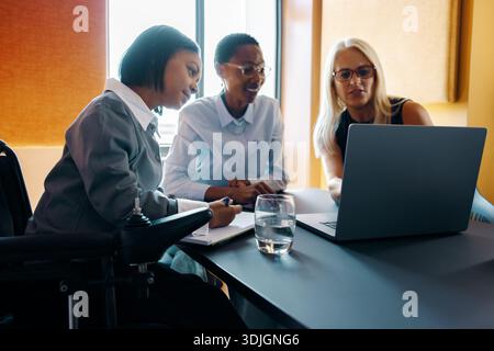 Tre colleghe di età diverse partecipano a una riunione sul posto di lavoro, utilizzando un notebook per scopi collaborativi in un ambiente contemporaneo Foto Stock