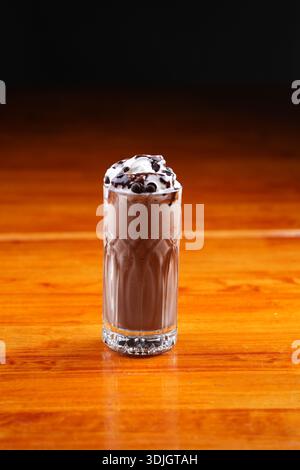 Cremoso milkshake al cioccolato con panna montata e gocce di cioccolato, presentato in un bicchiere a sfera alta testurizzato. Foto Stock