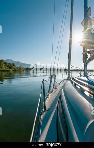 Barca a vela ancorata sul lago Chiemsee sullo sfondo delle Alpi, retroilluminata dal sole, Baviera, Germania Foto Stock