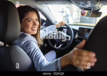 Giovane donna felice che prova la nuova auto prima di acquistarla nel salone dello showroom, concept acquista il primo veicolo. Eseguire una prova su strada del veicolo nuovo Foto Stock