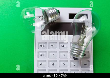Calcolatrice con lampadina a incandescenza su sfondo verde. Piatto a risparmio energetico Foto Stock
