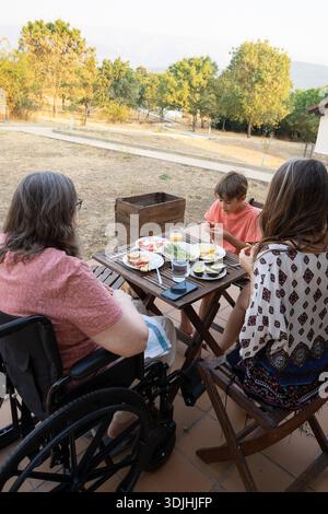 Membri della famiglia che mangiano cibo sano a un tavolo di legno su un patio durante l'estate Foto Stock