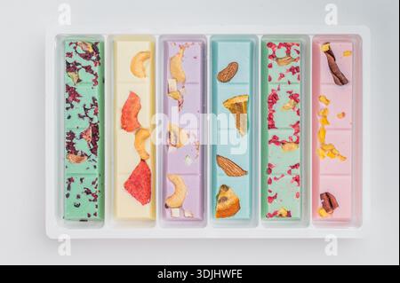 Colorate tavolette di cioccolato artigianale con frutta secca e noci su sfondo bianco, dolciumi artigianali fatti a mano, vista dall'alto. Foto Stock