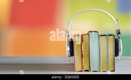 audiolibri, podcast, ascoltare il concetto di letteratura. Fila di libri con cuffie vintage e colori sfocati sullo sfondo. Panoramica con grande Foto Stock