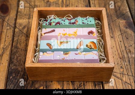 Collezione di tavolette di cioccolato artigianali disposte in scatola di legno con riempitivo di paglia su fondo in legno vintage dolci di prima qualità. Foto Stock