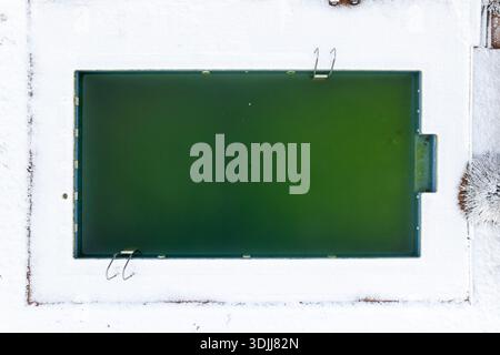 Foto di una piscina rettangolare circondata dalla neve che mostra una mancanza di manutenzione Foto Stock