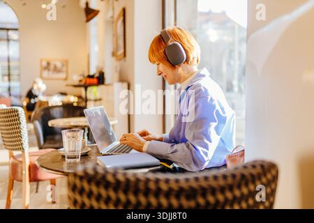 Donna freelance che lavora su un notebook al tavolo del bar, vista profilo Foto Stock