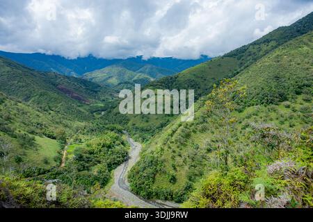 Lussureggianti e verdi pendii montani e vallata con un fiume roccioso che scorre sotto cieli nuvolosi Foto Stock