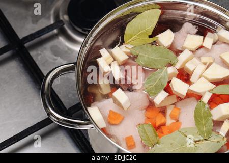 Cottura di zuppe fatte in casa su un piano cottura. Pentola con verdure e carne sospese nel brodo. Tradizionale processo di cucina casalinga. Cibo sano e confortevole. Foto Stock