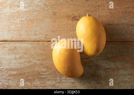 due manghi gialli maturi su una superficie rustica in legno, frutti della pelle lisci su motivo a grana di legno testurizzata, vista dall'alto con spazio di copia, cibo sano e tropico Foto Stock
