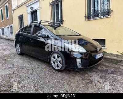 Toyota Prius nera / auto ibrida. Automobile, veicolo per pendolari. Parcheggiato su una strada sterrata e acciottolata nello storico quartiere Plaka di Atene, Grecia. Foto Stock
