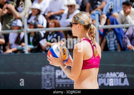 Atleta femminile di Beach volley che tiene la palla prima del servizio durante un torneo professionale con il pubblico in sottofondo. Foto Stock