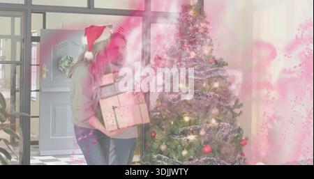 Portare regali, coppia anziana in casa, donna che indossa il cappello rosso di Babbo Natale, albero decorato Foto Stock