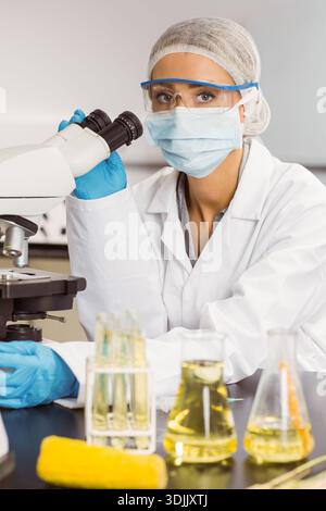 Microscopio composto posizionato su banco nero con provette beute e panno giallo nelle vicinanze. Laboratorio, scienziato, tecnico, occhiali, maschera, Foto Stock