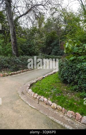Giardino nazionale di Atene, Εθνικός Κήπος (o Giardini reali). Percorso tortuoso delimitato da pietre, alberi lussureggianti e fogliame nel centro di Atene, Grecia. Foto Stock