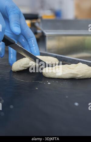 Una persona con i guanti taglia l'impasto con un coltello nella panetteria, panini da forno, Haselstaller Hof, Gechingen, Germania Foto Stock