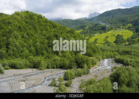 Pittoresco paesaggio con un fiume che scorre attraverso foreste e montagne ondulate sotto il cielo nuvoloso, la regione di Racha-Lechkhumi e il basso Svaneti, l'alto Cauc Foto Stock