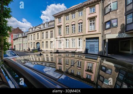 Edifici classici sulla strada Muelheimer Freiheit di Colonia, riflessi sul tetto di un'auto sotto un cielo estivo blu Foto Stock
