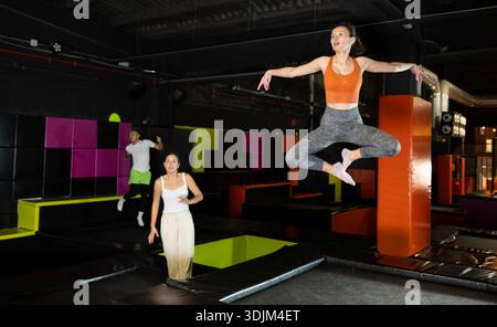 Donna di mezza età felice che pratica e salta sui trampolini in un centro sportivo al coperto, allenamento e moderno concetto di intrattenimento Foto Stock