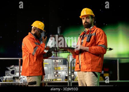 Il lavoratore della piattaforma offshore utilizza il software per laptop durante la notte di aurora boreale per prevedere le esigenze di manutenzione degli attrezzi. Gli esperti analizzano i dati sul cruscotto dei notebook sotto l'aurora boreale per evitare errori Foto Stock