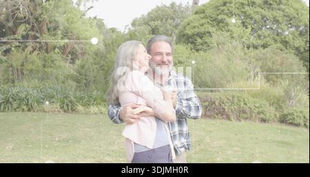 Abbracciare una coppia matura in piedi sul prato del parco, indossando cardigan e camicia a quadri Foto Stock