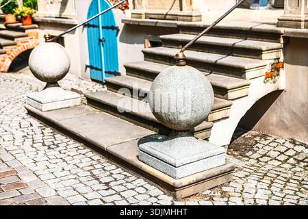 Affascinante scena di strada a Danzica, Polonia, con caratteristiche scalinate in perron e pavimentazioni in ciottoli. Le sfere di pietra e la porta blu vibrante Foto Stock