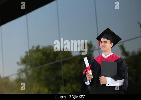 Studente laureato con diploma e libro vicino all'università Foto Stock