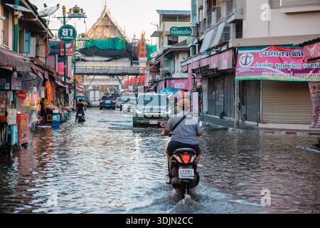 Mercato ferroviario di Maeklong in Thailandia, 5 dicembre 2025, l'acqua inonda le strade mentre le persone in moto viaggiano attraverso le strade allagate durante il clima Foto Stock