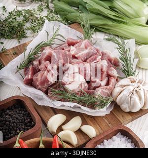 Assortimento di carne cruda, erbe fresche, spezie e verdure disposte su un tagliere di legno, pronte per la cottura. Foto Stock