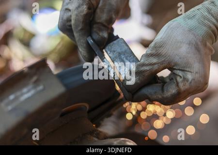 Lama in metallo abrasivo per fabbro con levigatrice a nastro in officina. Questo mestiere industriale mostra un lavoratore esperto che crea una pioggia di scintille con carefu Foto Stock