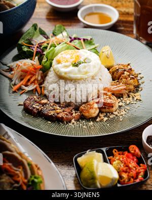 Primo piano di un tradizionale piatto vietnamita Com Tam, con riso rotto e un uovo soleggiato. Accompagnato da carne di maiale grigliata, succulento shr Foto Stock