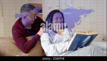 Una donna grigia ridendo che legge un libro sul divano di casa, un uomo che si appoggia in maglia marrone sotto una copertura viola Foto Stock