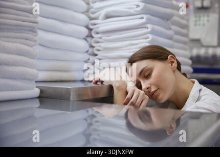 Una donna dorme tranquillamente di fronte a una grande pila di asciugamani Foto Stock