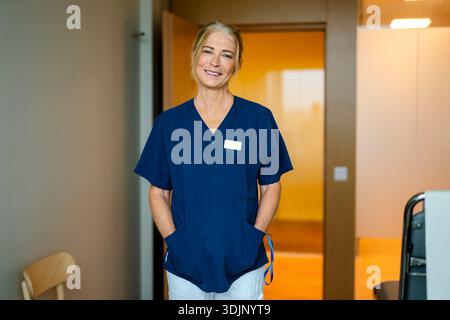 Ritratto di donna anziana sorridente medico in piedi con le mani in tasche a clinica Foto Stock