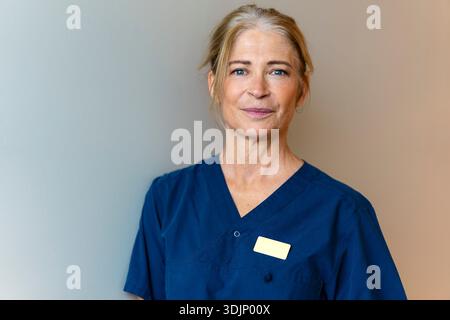 Ritratto di un medico anziano sorridente che indossa scrub contro il muro Foto Stock