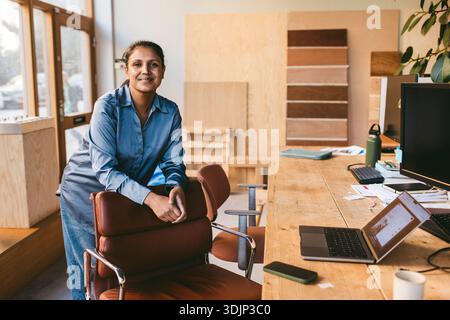 Ritratto di un professionista creativo e maturo appoggiato su una sedia vicino alla scrivania in ufficio Foto Stock