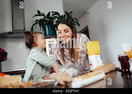Un bambino e una madre condividono un momento di gioia mentre cucinano nella loro cucina. Mescolano ingredienti, si divertono a vicenda e creano ricordi mentre p Foto Stock