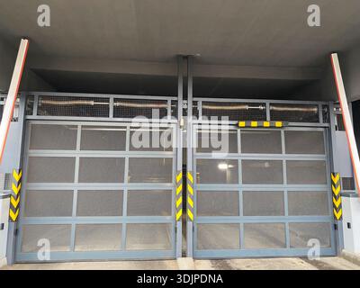 Le moderne porte di garage industriali sono dotate di pannelli a rete e strisce di attenzione, che forniscono un elemento di design funzionale in una spaziosa area di parcheggio commerciale wi-fi Foto Stock