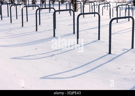 Parcheggio per biciclette coperto dalla neve con portabiciclette in metallo vuoto che getta lunghe ombre alla luce solare invernale. Foto Stock