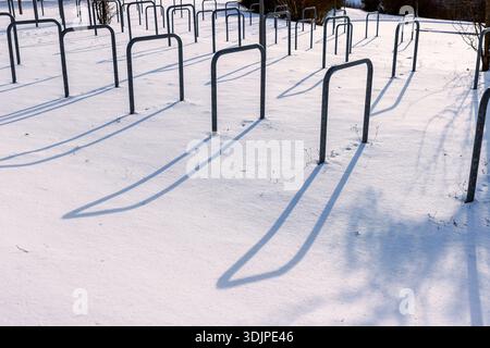 Parcheggio per biciclette coperto dalla neve con portabiciclette in metallo vuoto che getta lunghe ombre alla luce solare invernale. Foto Stock