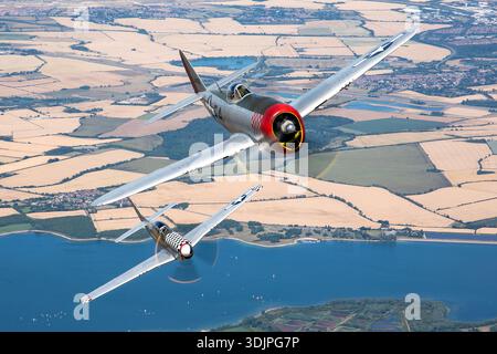 In questa immagine Air-to-Air del Regno Unito Warbirds 2022, Republic P-47D Thunderbolt 'Nellie B' e North American P-51D Mustang 'Converse Mary' sono mostrati nella livrea dell'aeronautica statunitense. Il P-47D utilizza un motore radiale Pratt & Whitney R-2800, mentre il P-51D è equipaggiato con un Rolls-Royce Merlin V12 costruito dalla Packard. La foto cattura la formazione volando con marcature dettagliate, coperture a bolle d'aria, eliche e superfici di controllo, sottolineando le caratteristiche dei caccia monoposto della seconda guerra mondiale. Foto Stock