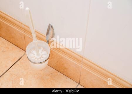Lo spazzolino per WC è collocato in un supporto a parete, posizionato su piastrelle beige con piastrelle bianche in bagno, evidenziando l'igiene e l'organizzazione Foto Stock
