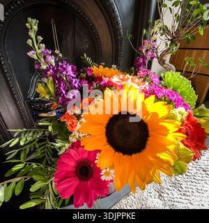 Mazzo misto luminoso di girasoli, gerberas, rose e altri fiori colorati disposti di fronte a un tradizionale caminetto in ghisa nera in un ambiente intimo Foto Stock