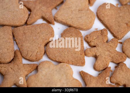 biscotti primi piani con cuore stellato su sfondo bianco, biscotti allo zenzero fatti in casa dorati in forme assortite, bordi morbidi con sottile consistenza alla cannella, caldi Foto Stock