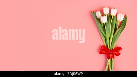 Appiattire un bellissimo bouquet di tulipani bianchi legati a un nastro rosso isolato su uno sfondo rosa pastello con spazio immacolato. oggetto per decorazione da donna Foto Stock