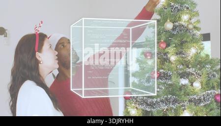 Uomo con cappello di Babbo Natale e donna con fascia di renna che decora l'albero di Natale a casa, copertura a cubo Foto Stock