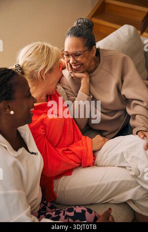 Vista dall'alto di una donna matura felice che guarda con affetto un'amica mentre si siede sul divano Foto Stock